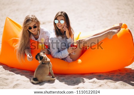 Two girls with coctails and small dog lying on pool mattress