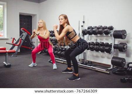 Two girls crouch in the gym, on their hands are smart watches. The concept of body fitness, sports in clothing overalls