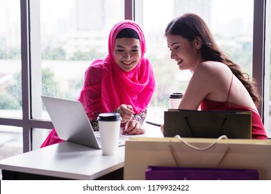 Two Girls Different Culture Are Talking About Business. They Look Happy Together. Islam Girl In This Pink Hijab And Dress Make Her Look Beautiful. And Girl In Red Dress Looks Very Elegant.