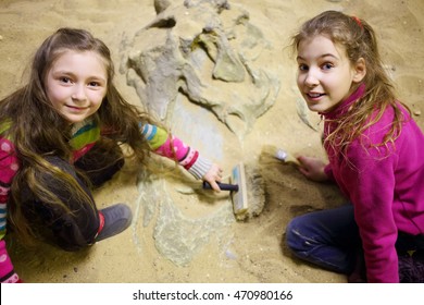 Two girls dig together in dry sand bones of dinosaur in sand