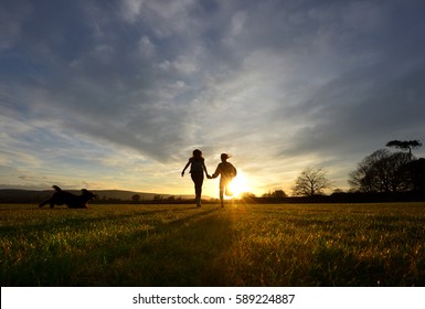 Two Girls And A Dog Running Into The Sunset