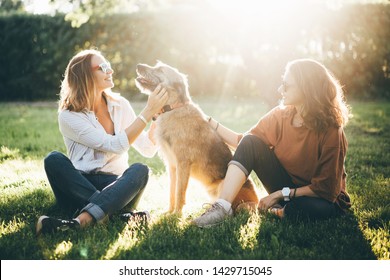 Two girls and dog sitting in the park at the sun set. And enjoying time together - Powered by Shutterstock