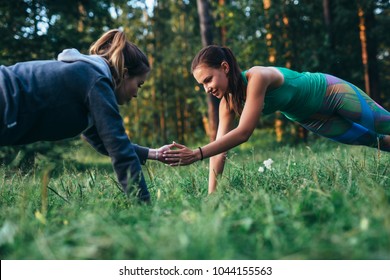 Two girls doing buddy workout outdoors performing push-ups to clap on grass