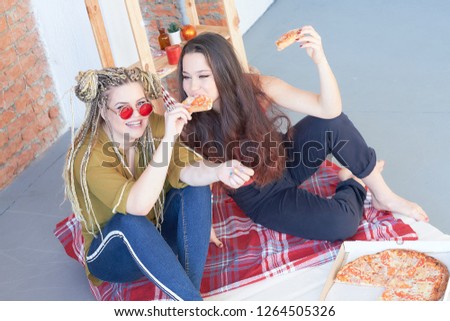 two girls eat pizza in the room on the bed. junk food.