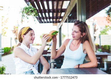 Two Girls Eating Burgers In A Street Cafe