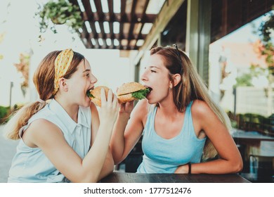 Two Girls Eating Burgers In A Street Cafe