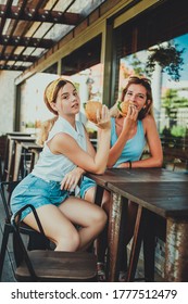 Two Girls Eating Burgers In A Street Cafe