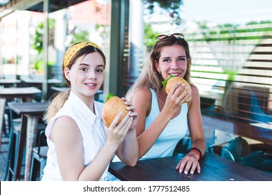 Two Girls Eating Burgers In A Street Cafe