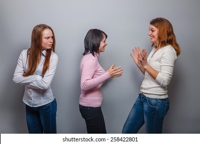 two girls European appearance blonde and brunette laugh and ignore the third girlfriend on a gray background, resentment, anger - Shutterstock ID 258422801
