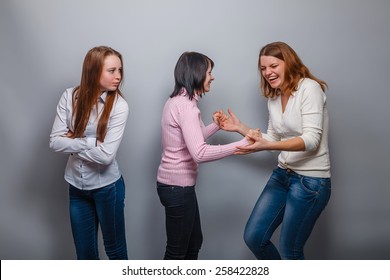 two girls European appearance blonde and brunette laugh and ignore the third girlfriend on a gray background, resentment, envy - Shutterstock ID 258422828