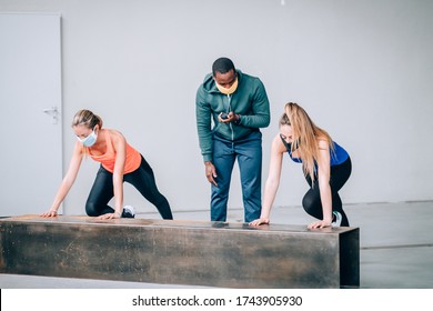 Two Girls Exercising With A Personal Trainer At The Gym With Protective Mask In Pandemic Period Of Covid19 - Two Fit Young Girls In A Gym Doing Squats With Their Trainer