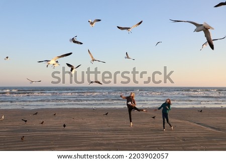 Two girls feeding flying seagulls on the beach