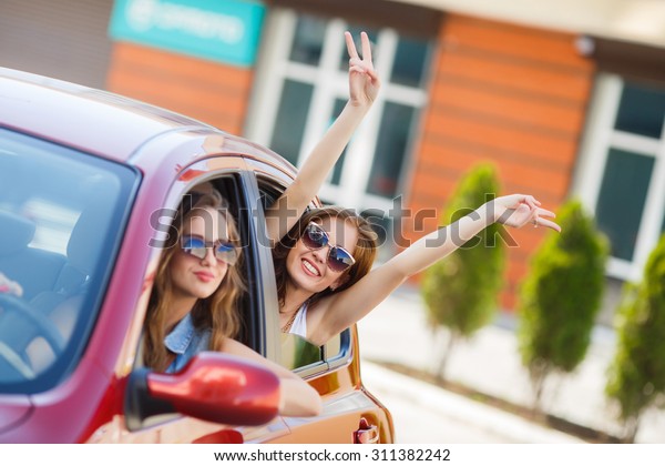 two girls friends in car. summer vacation. Friends\
going on road trip travel on summer day. freedom. cheering joyful\
with arms raised