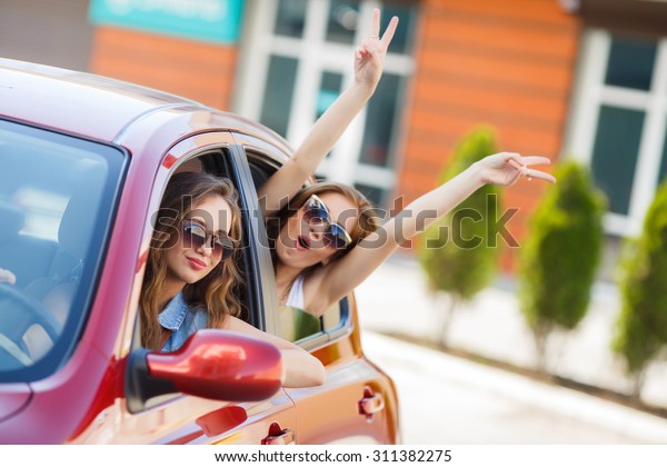 two girls friends in car. summer vacation. Friends\
going on road trip travel on summer day. freedom. cheering joyful\
with arms raised