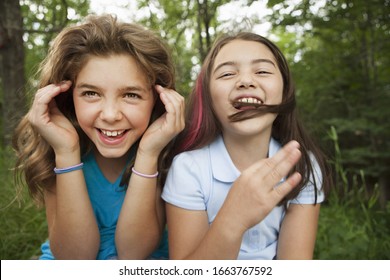 Two Girls, Friends Sitting Side By Side, Playing And Laughing.