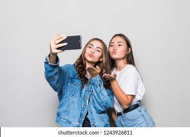 Two Girls Friends Taking Selfie With Smartphone, Blowing A Kiss In The Camera, Isolated On White Background