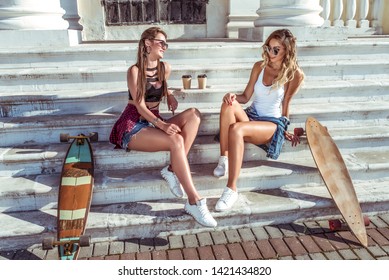 Two girls girlfriends, sitting on the stairs in summer in city, talking talk, happy laugh and smile, skateboard, cups of coffee, beautiful and tanned figures. Concept best friends girlfriend. - Powered by Shutterstock