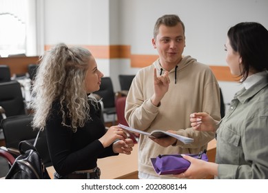 Zwei Mädchen und ein Typ sprechen in Gebärdensprache. Drei taube Schüler plaudern in einem Klassenzimmer.