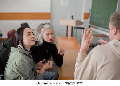 Two Girls And A Guy Are Talking In Sign Language. Three Deaf Students Chatting In A University Classroom.