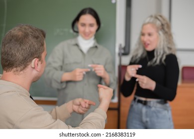 Two Girls And A Guy Are Talking In Sign Language. Three Deaf Students Chatting In A University Classroom.