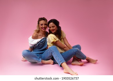 Two Girls Have Fun And Posing Against The Pink Studio Background. Happy Friends Dressed Fashion T-shirt And Jeans.