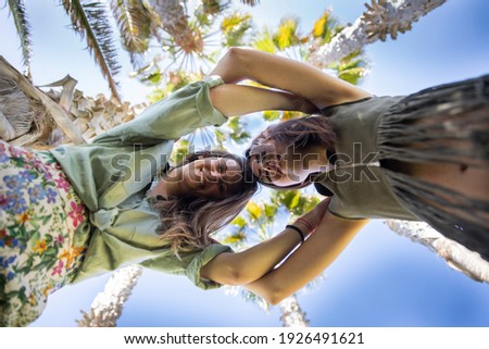 Two girls have fun while on vacation in an exotic location with palm trees. Photo taken from below. Head to head pose