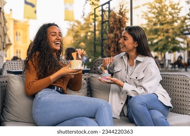 Two girls are having fun and eating delicious ice-cream in the cafe garden on a sunny day. - Powered by Shutterstock