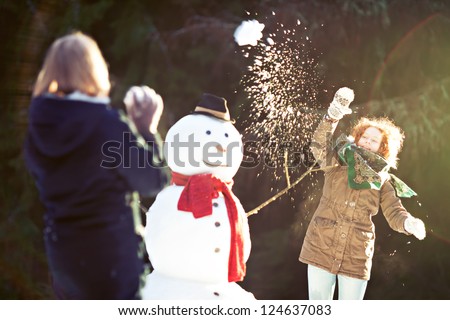 Two girls having snowball fight. One of them throwing snowball is in focus, motion blur