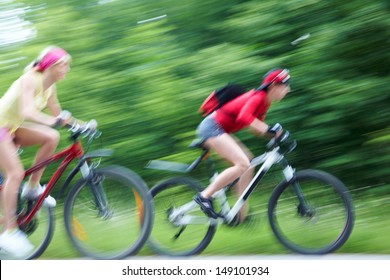 Two Girls At A High Speed Chase On Bicycles On Green Park