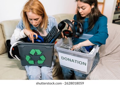 Dos niñas sostienen una caja con partes de computadoras viejas, preparándose para reciclarlas o donarlas.