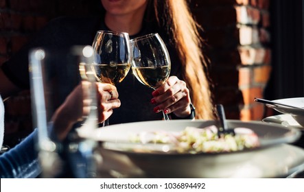 Two girls are holding glasses of white wine at the dinner table, golden hour, horizontal composition

