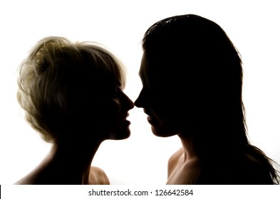 Two Girls Kissing In Front Of A White Wall.