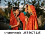 Two girls in Kumaoni traditional attire adjusting their dress, preparing for a vibrant celebration of culture and tradition.