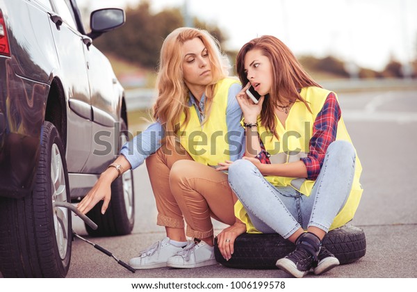 Two girls on the road trying to fix their\
car.Changing tire on broken car on\
road.