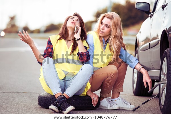 Two girls on the road trying to fix their\
car.Changing tire on broken car on\
road.