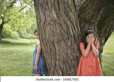 Two Girls Playing Hide And Seek By Tree In Park