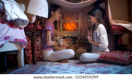 Two girls playing in selfmade tent and telling stories at night