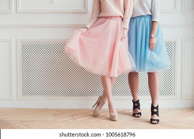 Two girls are posing for a photo. They are showing their legs, folding skirts a wearing high heels. Celebration of the party.