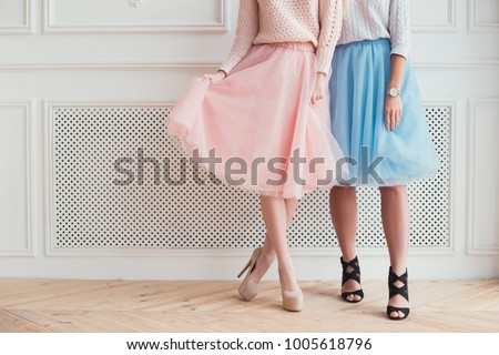 Two girls are posing for a photo. They are showing their legs, folding skirts a wearing high heels. Celebration of the party.