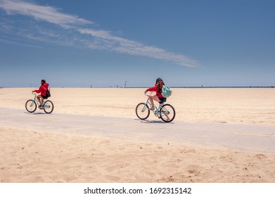 Two Girls Riding Bicycles On A Beach Bike Path Under A Blue Sky