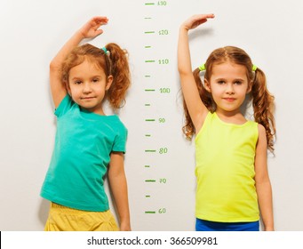 Two Girls Show Height On Wall Scale At Home