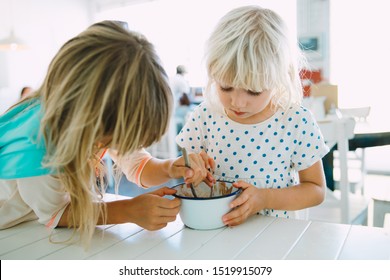 Two Girls Sisters Eating Ice Cream From One Bowl In A Cafe Indoors