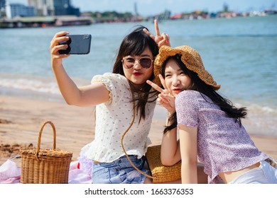 Two girls sitting on the beach at the sea in sunny day, take a selfie together and making duck face. - Powered by Shutterstock