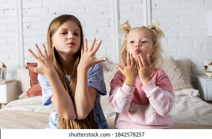 Two girls are sitting on the bed in the bedroom and showing off their new manicure.