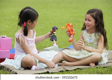 Two Girls Sitting On Picnic Blanket, Playing With Dolls