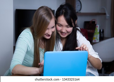 Two girls sitting at a table in front of the computer. They choose to shop online.