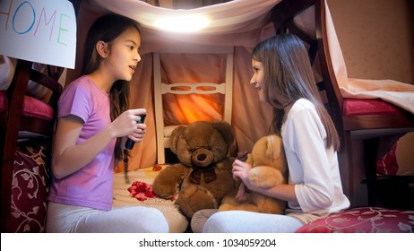 Two Girls Sitting In Tent Made Of Blankets And Telling Stories