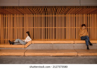 Two Girls Sitting In A Wooden Pavillion And Looking Busy