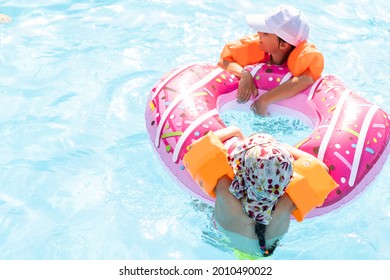 Two Girls Splash In An Outdoors Swimming Pool In Summer. Happy Children, Sister Playing, Enjoying Sunny Weather In Public Pool