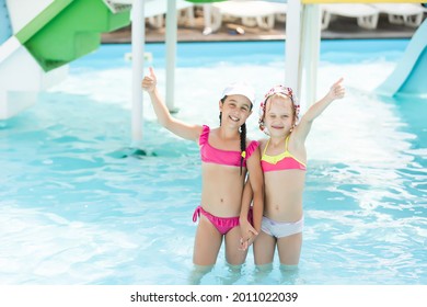 Two Girls Splash In An Outdoors Swimming Pool In Summer. Happy Children, Sister Playing, Enjoying Sunny Weather In Public Pool